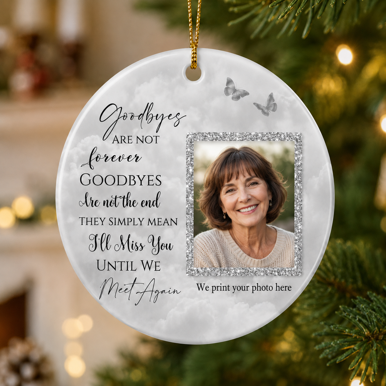 A round hanging Christmas ornament with a printed photo frame placeholder and sentimental text, shown hanging on a blurred Christmas tree with warm lights in the background.