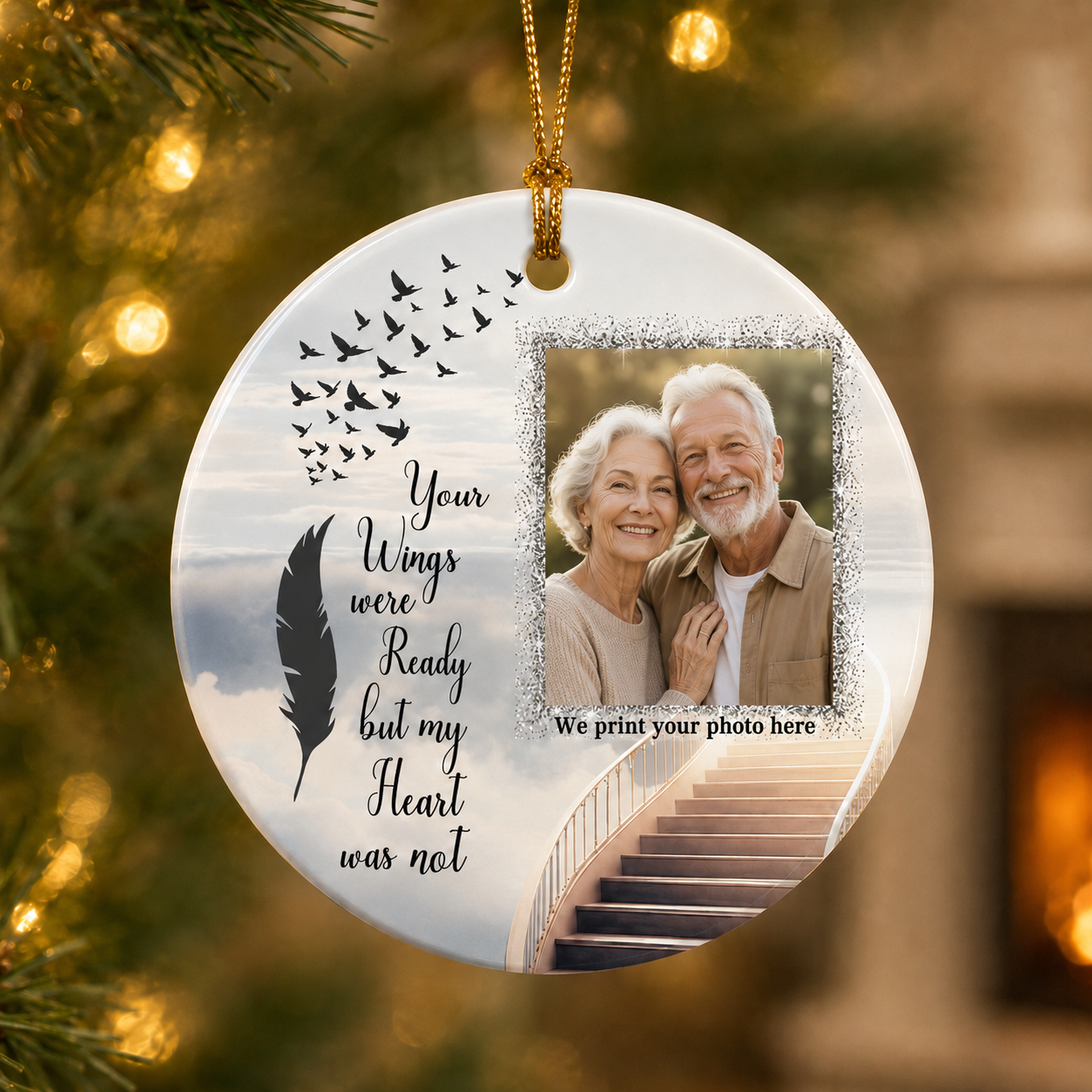 A round hanging memorial ornament with a photo of an elderly couple, black bird silhouettes, a feather graphic, and the text 'Your Wings were Ready but my Heart was not,' shown hanging in front of a blurred Christmas tree and warm indoor background.