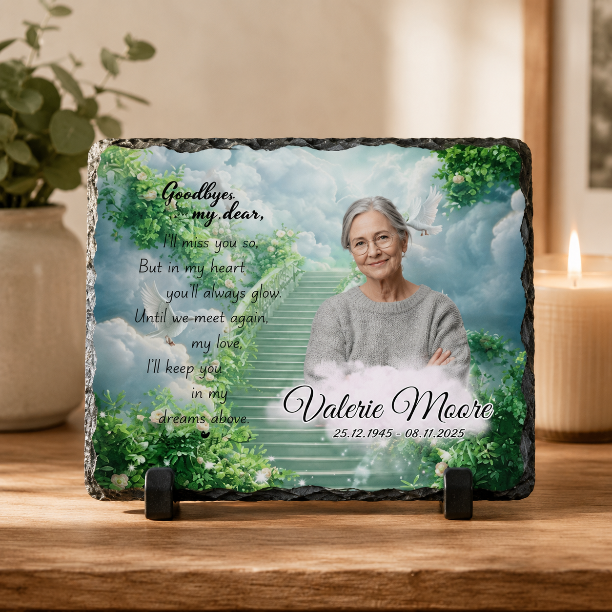 Personalized memorial slate plaque on a wooden surface, featuring a portrait of an elderly woman, a white staircase through clouds, green foliage, and the text 'Goodbye, my dear.