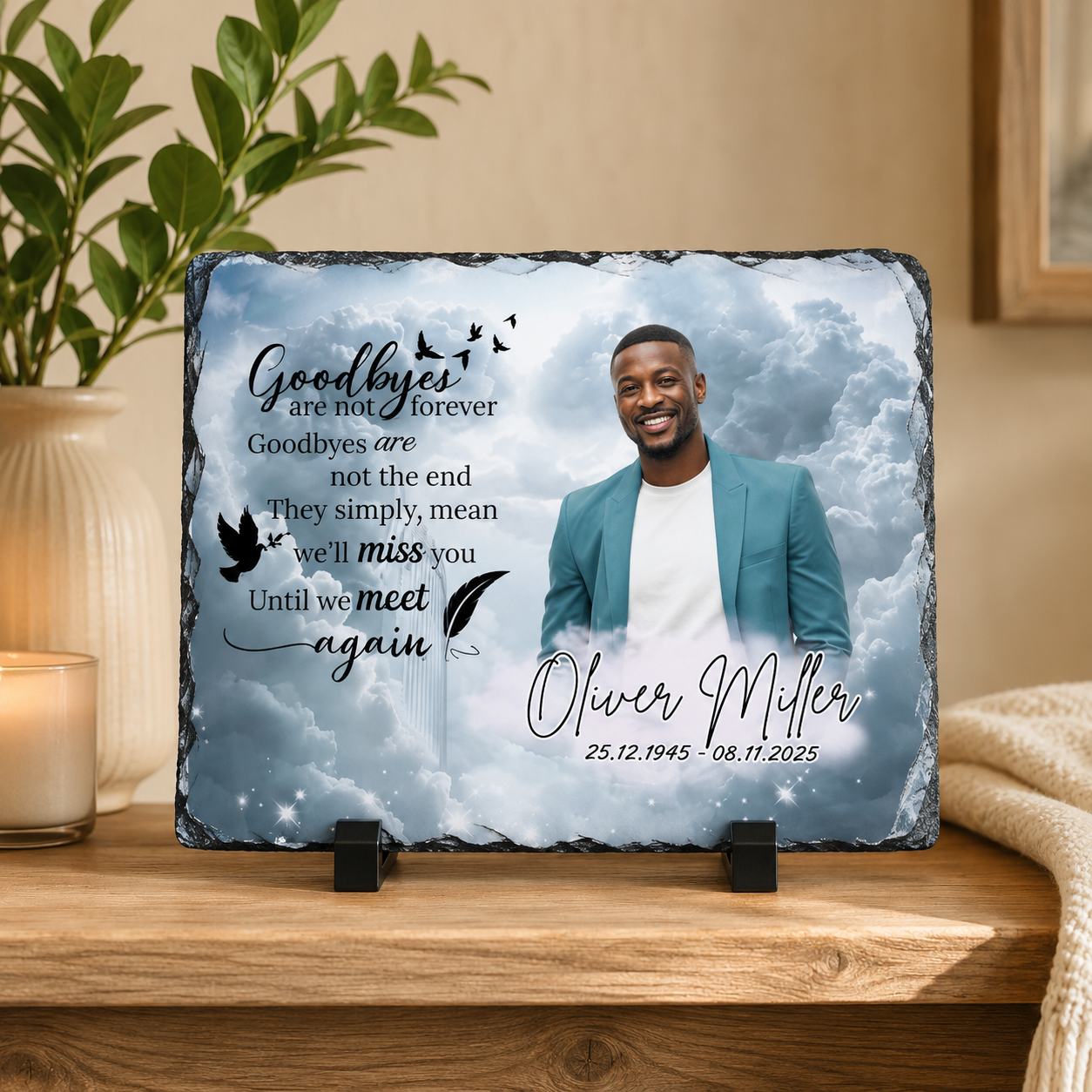 Personalized memorial slate plaque on a wooden table, featuring a photo of a man, cloudy background, black text reading 'Goodbyes are not forever' and the name 'Oliver Miller' with dates, displayed with two small black stands in a home setting.
