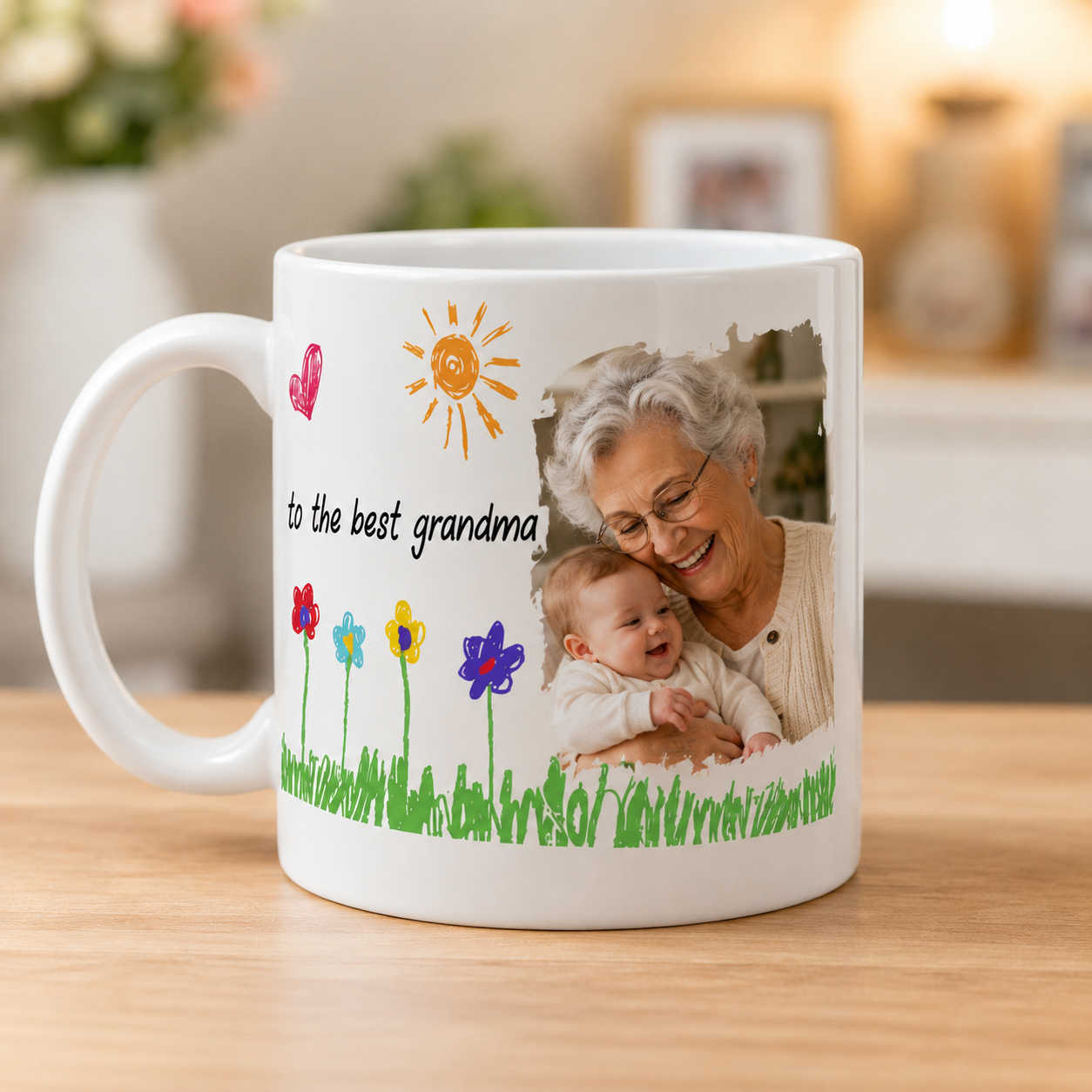 A white ceramic mug on a wooden table, featuring a custom photo of a smiling grandma and baby, a sun, colorful flowers, and the text 'to the best grandma'.