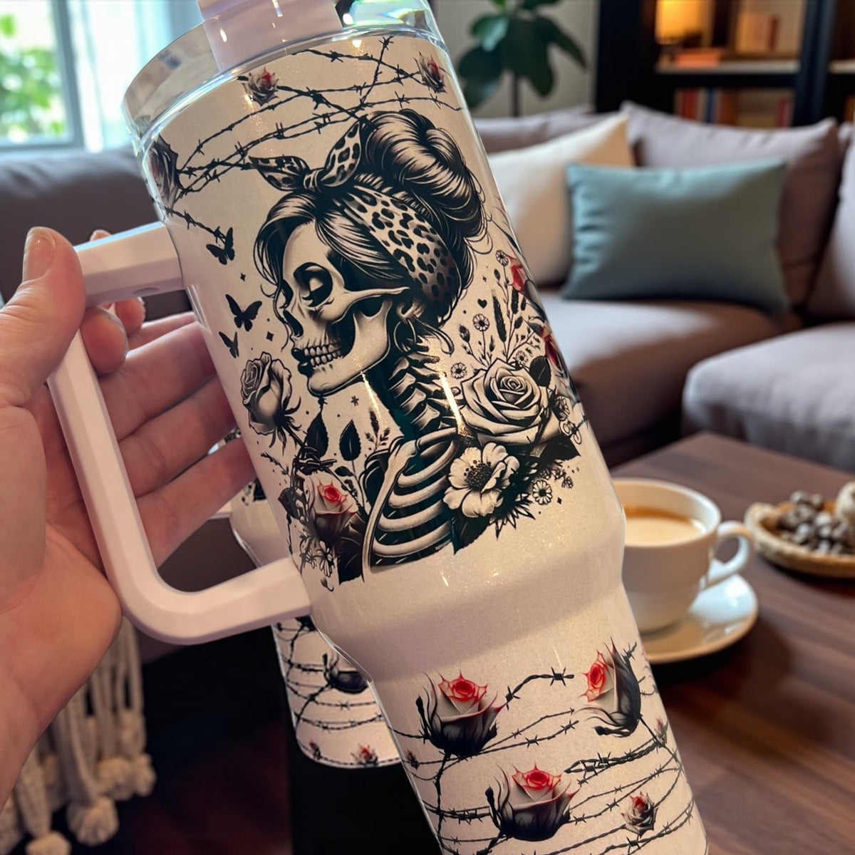 White mug with black and white skull design held by a hand, with a cozy living room background.