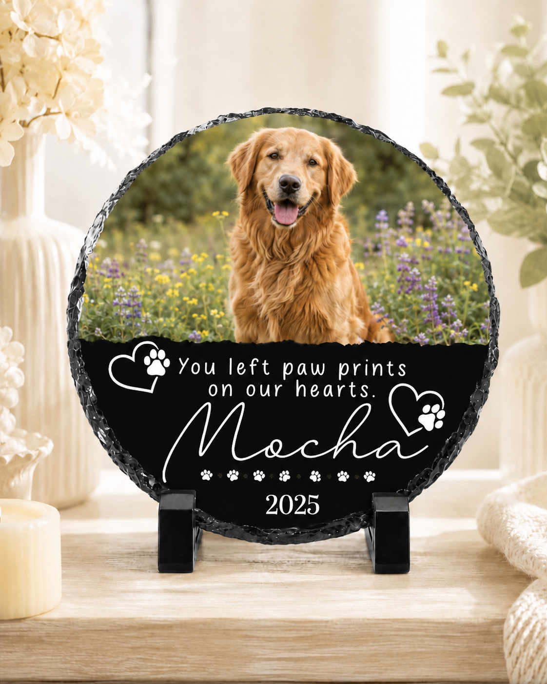 Personalized round slate memorial plaque on a small black stand, featuring a photo of a golden retriever in a field and engraved white text reading 'You left paw prints on our hearts Mocha 2025' on a black lower section.